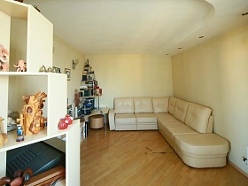 мягкий бежевый угловой диван в светлой гостиной трехкомнатной квартиры геолога в жилой многоэтажке