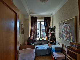 деревянные кроватки с голубым и розовым покрывалом, разноцветные коробки и комод у стены с яркой картиной в детской комнате стильной квартиры художника