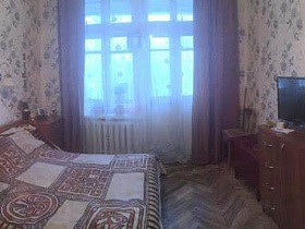цветочные бежевые стены спальной комнаты с коричневыми шторами на большом окне квартиры советского времени в хрущевке