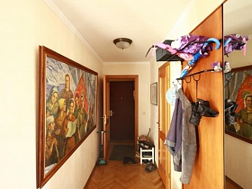 обувь на коврике у входной двери, обувная полка,мебельная деревянная стенка с зеркалом,большие картины эпохи СССР на стенах светлой прихожей квартиры художника