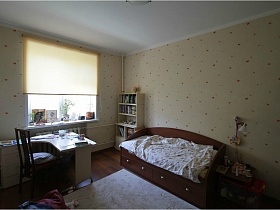 белый полугруглый компьютерный стол, белый открытый шкаф с книгами в углах спальни у окна с жалюзи в квартире педагога