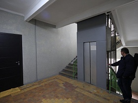 просторный светлый холл с плиткой на полу у входных дверей квартиры и дверей лифта, лестницей с перилами между этажами в жилом доме