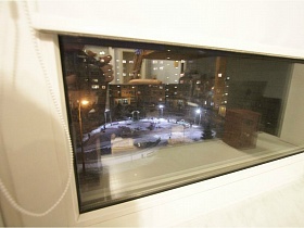 огни ночного города из окна детской комнаты с опущенными белыми жалюзи простой трехкомнатной квартиры