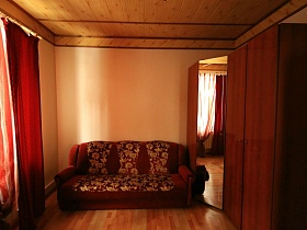 коричневый диван с бежевым рисунком, большой угловой шкаф с зеркальной дверцей в гостевой спальне пустого двухэтажного съемного дома в сосновом лесу