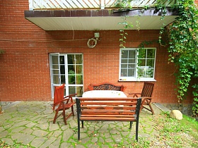 складные деревянные стулья и скамейки вокруг стола с клеенкой под балконом,у окна кирпичного двухэтажного дома в глухом лесу