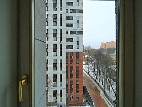 вид из окна на торец соседнего современного многоэтажного дома и брусчатую дорогу в красивом дворе новостроек