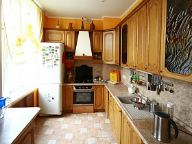 коричневая кухня с газовой плитой,вытяжкой, раковиной,рабочей поверхностью и белым холодильником у окна трехкомнатной квартиры №16