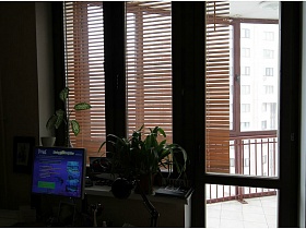 большой монитор на компьютерном столе, комнатные цветы на подоконнике окна с балконной дверью на большую мансарду простой двухкомнатной квартиры для съемок кино