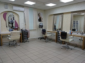 оборудованные рабочие места мастеров современного салона парикмахерской 2 с уютными креслами для клиентов, деревянными столиками, серыми тележками и зеркалами в нишах светлых стен