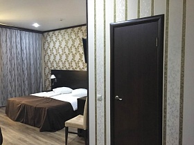 темно коричневая дверь санкомнаты в современном номере гостиницы с аккуратно заправленными кроватями у высокого изголовья на полу с бежево коричневым линолеумом под дерево