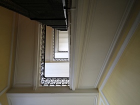 вид снизу на белый лестничные пролеты с резными металлическими перилами на ступенях в ухоженном подъезде жилого дома эпохи СССР