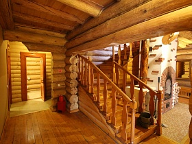 деревянная лестница с резными перилами вокруг белой стилизованной русской печи с кирпичной отделкой на второй этаж деревянного дома