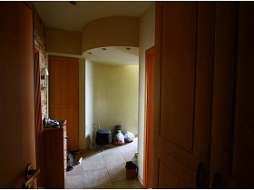 коричневый комод, пакеты с мусором, ведро с крышкой на полу с квадратной плиткой в светлом коридоре с подвесным круглым потолком двухкомнатной квартиры с видом на Москва-сити