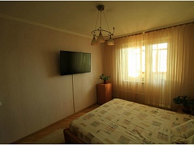 люстра с тремя бежевыми плафонами над кроватью в бежевой спальне трехкомнатной квартиры