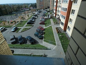чистый ухоженный двор с детской площадкой , газонами и машинами на парковочных местах жилой современной многоэтажки в зеленом массиве