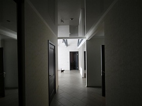 длинный светлый коридор с белой квадратной плиткой на полу и натяжным потолком красивого загородного дома в скандинавском стиле