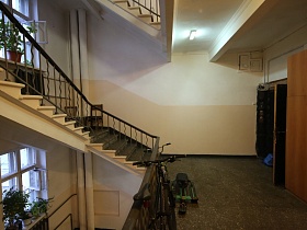 просторная лестничная площадка с жилыми квартирами, велосипедами у металлических перил многоступенчатой лестницы для съемок кино