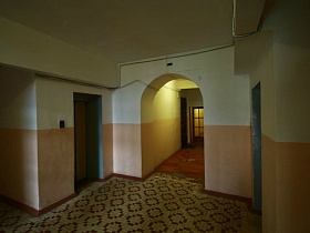белый потолок и стены просторного холла подъезда сталинского дома с лифтами и арочным дверным проемом в коридор с квартирами