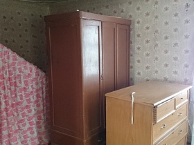 трехдверный коричневый шкаф, бежевый комод и цветочная ширма в комнате со светло серыми обоями дома заброшенной деревни