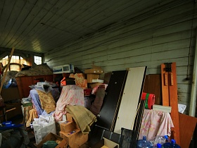 разобранная мебель, многочисленные коробки, ящики, вещи и бутыля для воды на полу деревянной веранды с зелеными стенами старинного дома в Ногинске