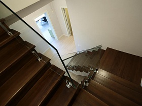 коричневые ступени лестницы между этажами со стеклянными перилами в загородном доме