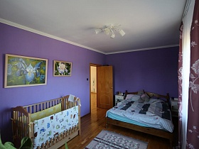 большая деревянная кровать, детский манеж, ковровая дорожка на полу спальной комнаты с яркими стенами и белым потолком семейной дачи с видом на город