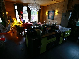 коричневый шкаф с салатовыми дверцами в зоне кухни просторной гостиной с камином в центре современного загородного дома для съемок кино