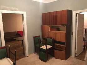 перевернутые стулья с зеленой обивкой, старый деревянный шкаф с антресолью в проходной комнате с серыми стенами и открытыми дверьми в соседние комнаты квартиры N6