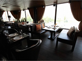 коричневые  деревянные столики с коричневыми диванами у больших окон с тяжелыми ораньжевыми шторами в ораньжевом зале уютного евро ресторана