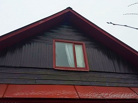 коричневый чердачный фасад деревянного домика в деревне с белой гардиной на прямоугольном окне