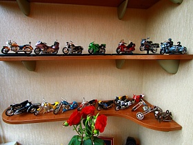 коллекция масштабных копий мотоциклов на открытых угловых деревянных полках на застекленной лождии квартиры государственного служащего
