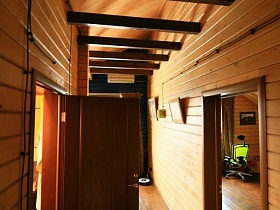 коричневые деревянные балки между деревянными стенами узкого длинного коридора в мансарде загородного дома
