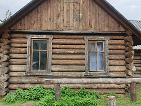деревянный бревенчатый дом под крышей с открытым крыльцом с перилами во дворе за забором в русской деревне для съемок кино