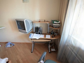 серый телевизор, компьтерный столик с полками у окна с белой гардиной спальной комнаты трехомнатной квартиры геолога в многоэтажном доме