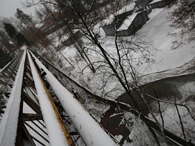 желтые огромные трубы, проходящие под высоким пешеходным подвесным мостом через реку, засыпанную снегом