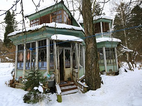 небольшая зеленая елочка у крыльца со ступенями под навесом деревянной двухэтажной дачи художника с овальной террасой советских времен