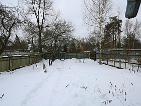 узкий длинный загороженный двор дачного участка в снегу