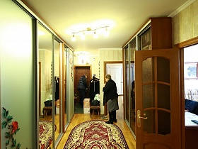 шкафы-купе у стен прихожей с цветным ковром  на полу в современной трехкомнатной квартиры врача