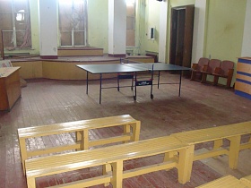 светлые новые деревянные скамейки, письменный стол, секционные кресла вокруг теннисного стола в комнате для занятий старого клуба советского времени