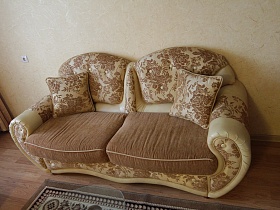 двухместный диван в бежево коричневом цвете с подушками у стены номера гостиницы