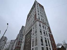 вид снизу на высокий многоэтажный современный светлый дом в серо-коричневой цветовой гамме во дворе новостроек