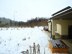 большой неухоженный участок красивого загородного дома под снегом