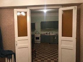 белая газовая плита между шкафами серо зеленой мебельной стенки на полу с шахматной плиткой кухни из открытых дверей квартиры на Остоженке