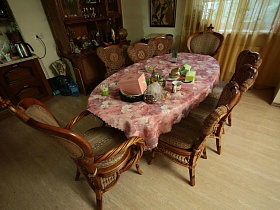 деревянные стулья со спинками вокруг стола с розовой скатертью в зоне кухни просторной комнаты семейного дома среди густого леса