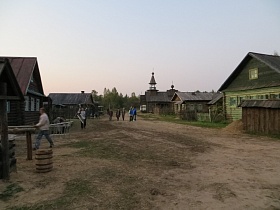жилые деревянные дома с хозяйственными постройками за невысоким забором вдоль широкой улицы большой деревни