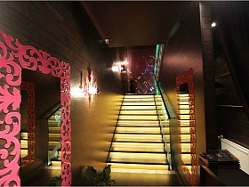 красочное оформление больших зеркал в холле евро ресторана у основания лестницы с подсветкой в белый и ораньжевый залы