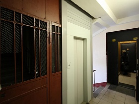 серая плитка на полу лестничной площадки с лифтом и общей дверью тамбура двух квартир на этаже девятиэтажного жилого дома
