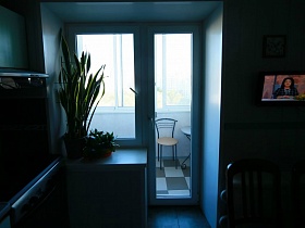 стул с металлической спинкой у круглого столика на застекленном балконе через закрытую балконную дверь из кухни квартиры оператора