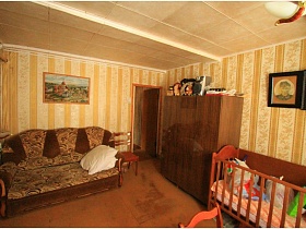 мягкий коричневый диван с подлокотниками, трех дверный шкаф и детская кроватка в просторном гостиной дачи