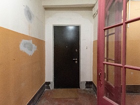 коврик у черной металлической двери в современную квартиру с элементами лофт из длинного коридора с белым побеленным потолком и окрашенными бежевыми обоями в сталинском доме
